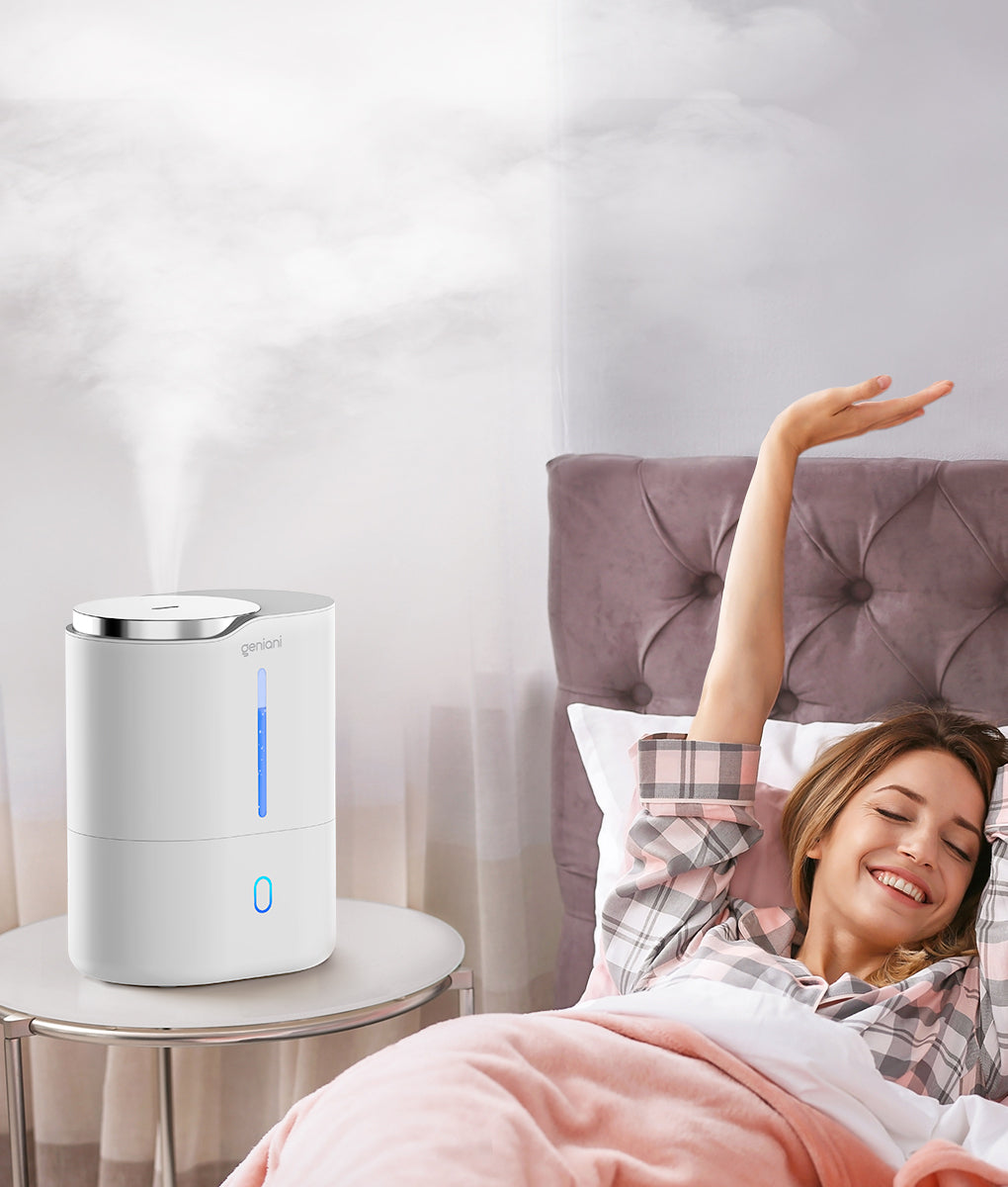 Quiet white bedroom humidifier releasing cool mist on bedside table next to smiling woman stretching in bed