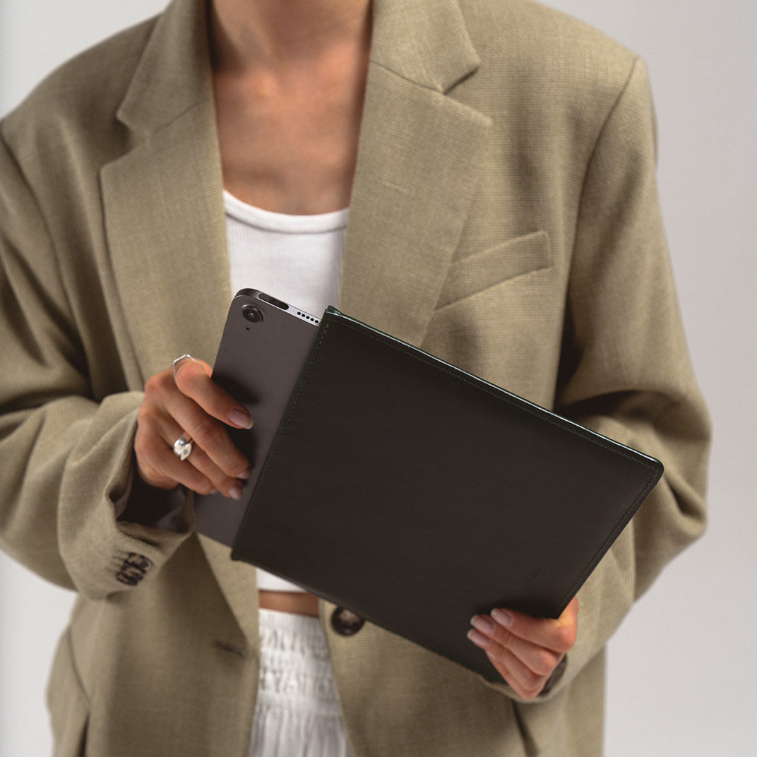Person holding a black slim leather sleeve for iPad, showcasing minimalist European handcrafted design and top-grain leather finish.