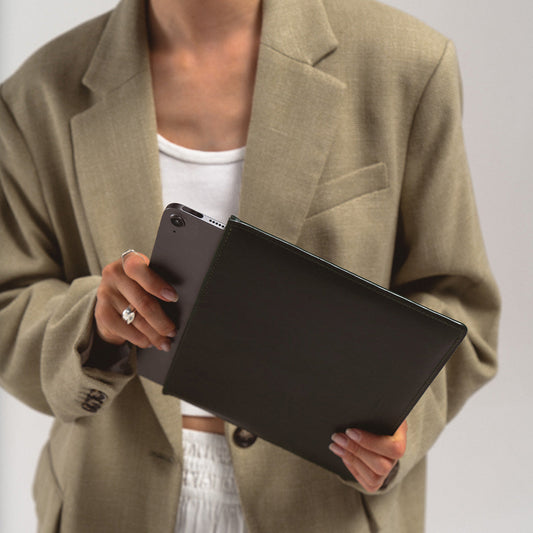 Person holding a black slim leather sleeve for iPad, showcasing minimalist European handcrafted design and top-grain leather finish.